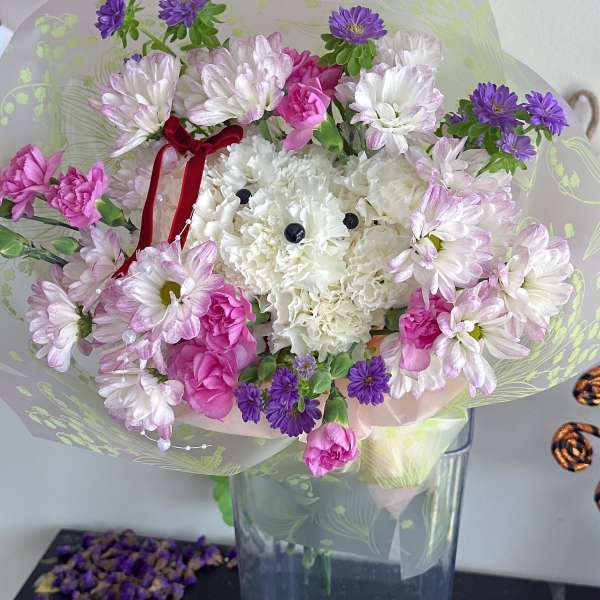 Bouquet of white, pink, and purple flowers in clear wrap with a red ribbon