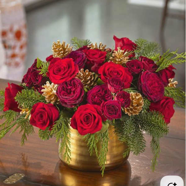 Red roses arranged in a gold vase with pinecones and evergreen sprigs