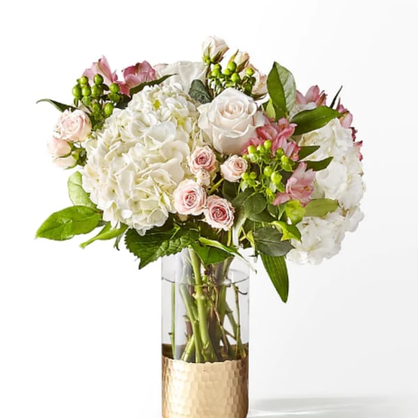 White and pink floral arrangement in a clear glass vase with a gold base