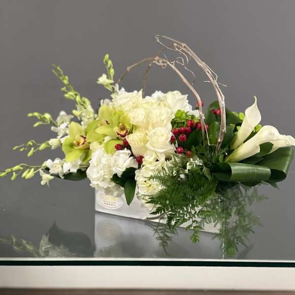 White and green floral arrangement with calla lilies and orchids in a white container