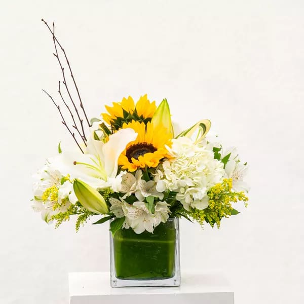 Sunflowers and white lilies in a square glass vase