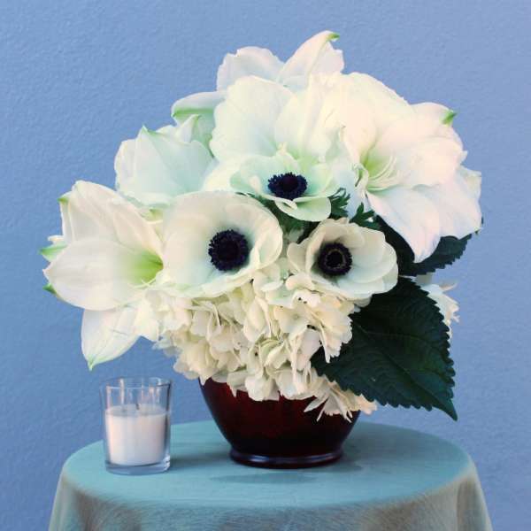 White floral arrangement in a dark vase beside a small candle