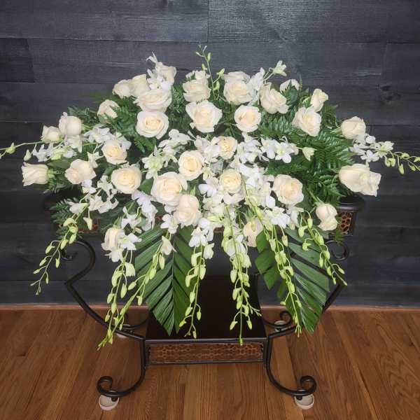 White roses and orchids arranged in a low black stand.
