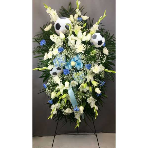 Standing floral spray with white flowers, blue accents, and soccer balls