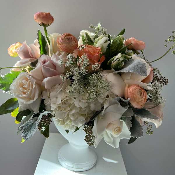 Blush and white floral arrangement in a white pedestal vase