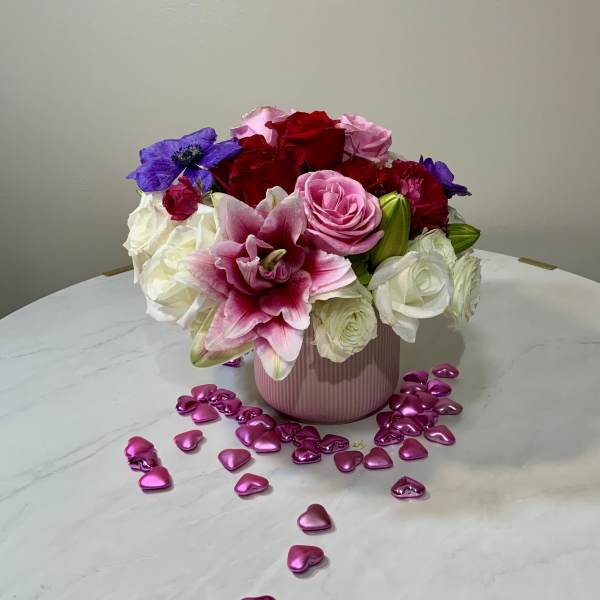 Bouquet of red, pink, white, and purple flowers in a pink vase with heart confetti