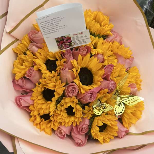 Bouquet of yellow sunflowers and pink roses wrapped in pale pink paper
