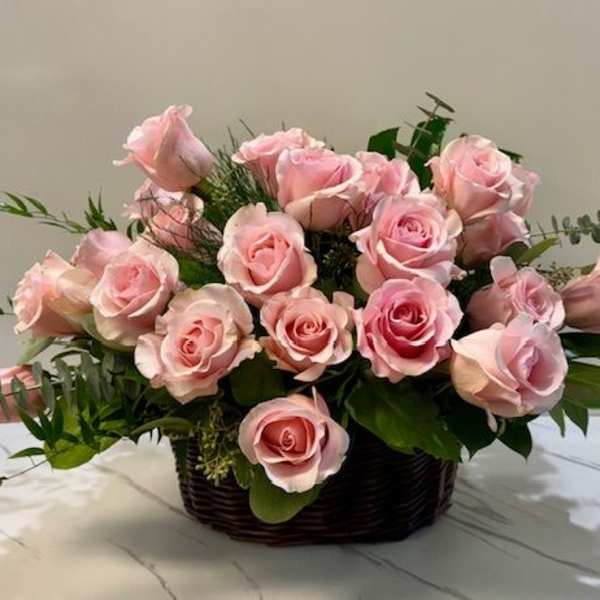 Pink roses arranged in a dark basket with greenery