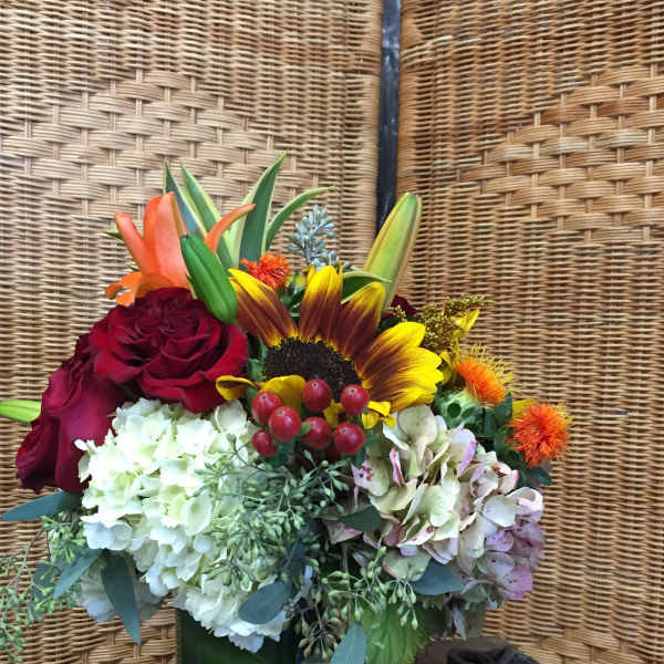 Mixed bouquet with roses, hydrangeas, and a sunflower in a green vase