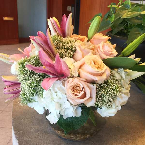 Bouquet of pink roses, lilies, and white hydrangeas in a glass bowl vase