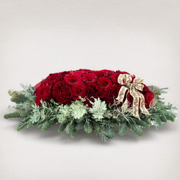 Red rose centerpiece with evergreen foliage and a decorative ribbon bow