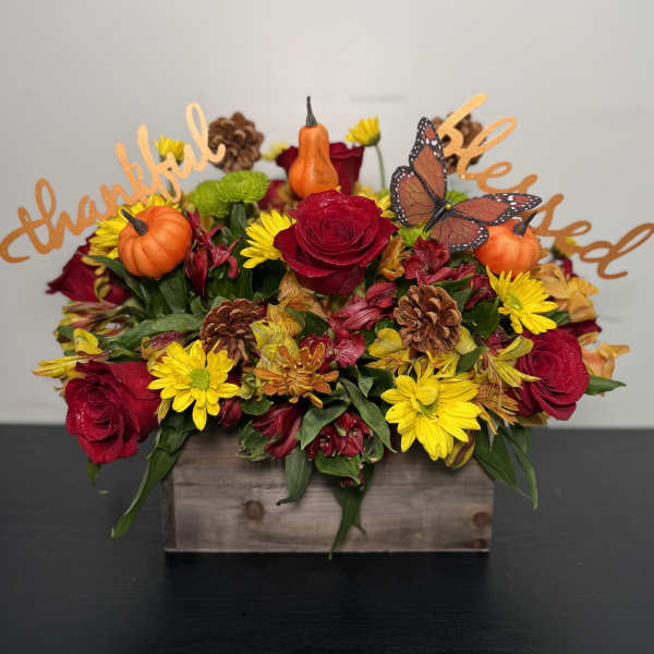 Fall floral arrangement with roses, daisies, pumpkins, and butterflies in a wooden box