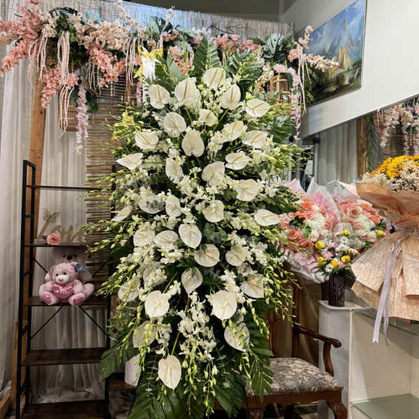 Large white floral standing arrangement with cascading orchids and anthuriums