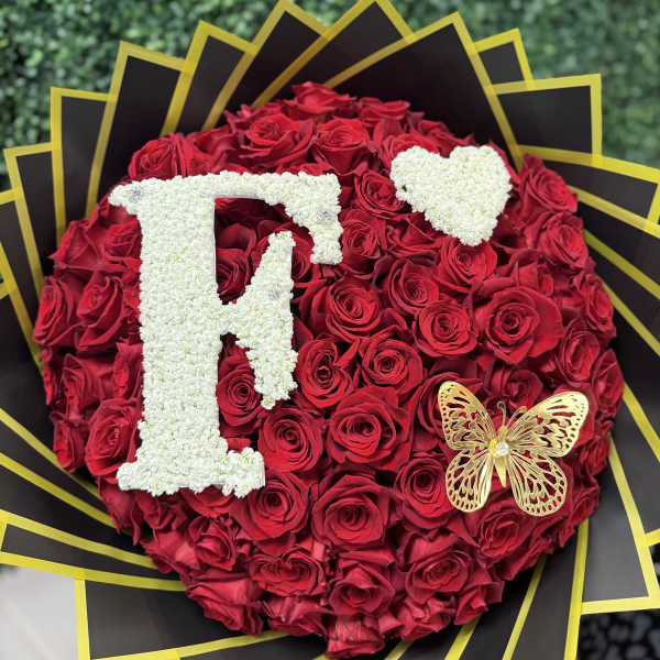 Heart-shaped bouquet of red roses with white floral initials and a butterfly accent