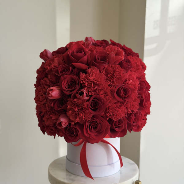 Round bouquet of red roses and carnations in a white box with a red ribbon
