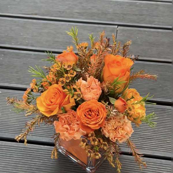 Orange roses and peach carnations in a clear square vase