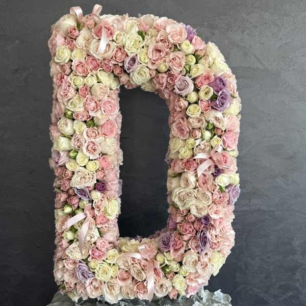 Large floral letter D covered in pastel roses and ribbons