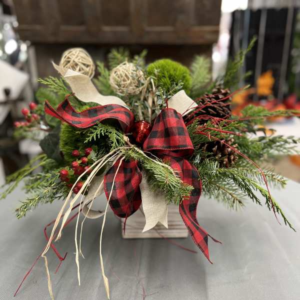 Holiday arrangement of evergreen branches with red plaid ribbon in a wooden container