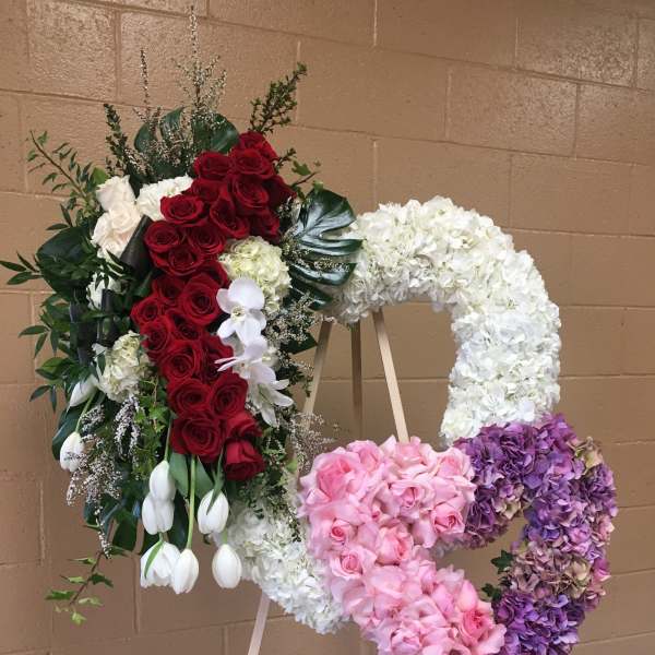 Heart-shaped floral wreath on an easel with red, white, pink, and purple flowers