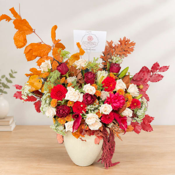Autumn floral arrangement in a cream vase with roses and red blooms