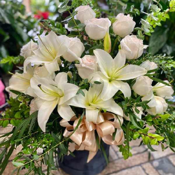 White lilies and pale roses in a dark vase with a satin ribbon