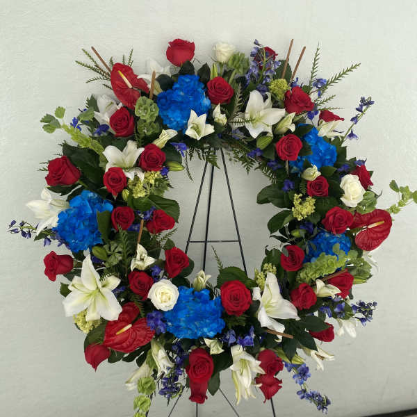 Circular wreath of red roses, white lilies, and blue hydrangeas on a stand