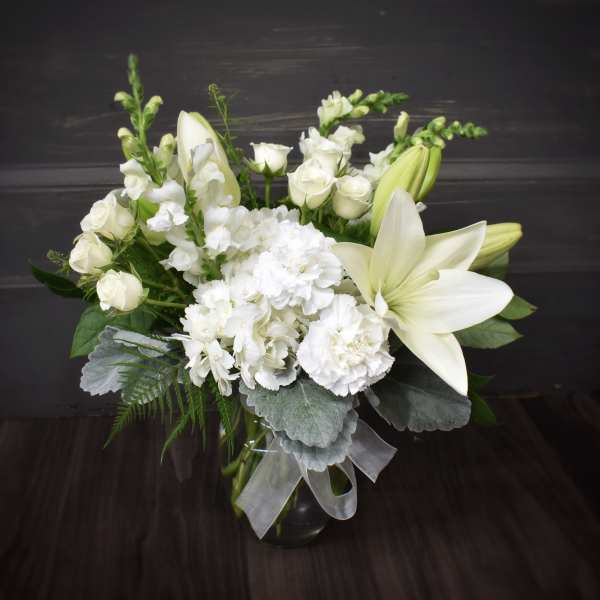 White lilies and roses arranged in a glass vase with silver ribbon