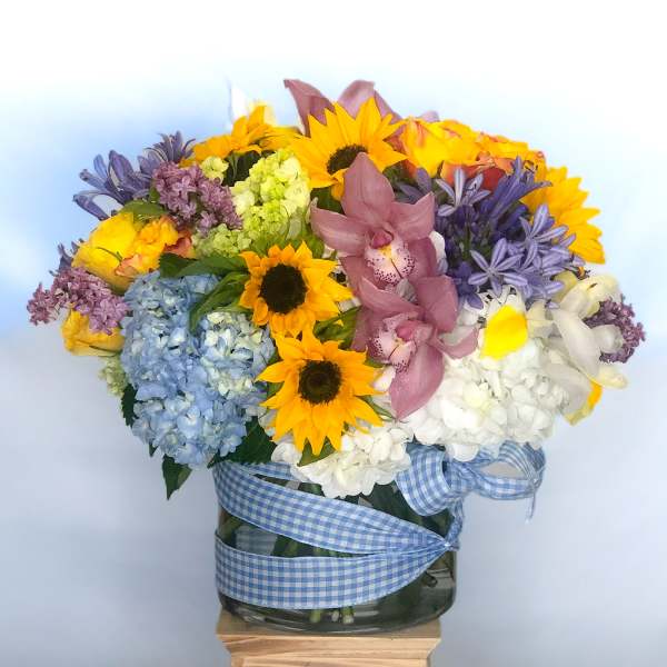 Mixed bouquet with sunflowers, hydrangeas, orchids, and a gingham ribbon in a glass vase