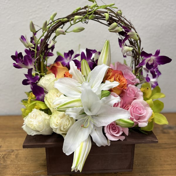 Basket arrangement with white lilies, pink and purple roses, and orchids