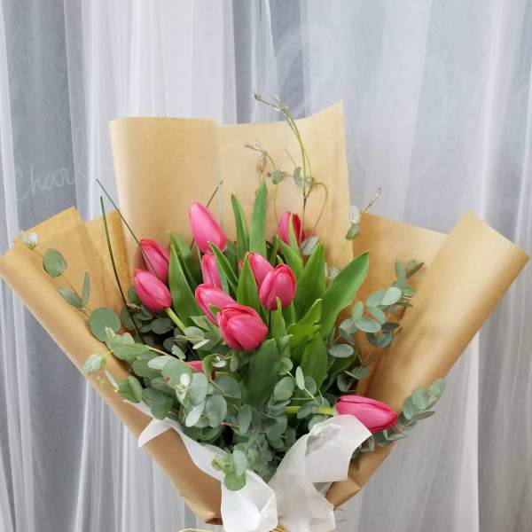 Pink tulip bouquet wrapped in brown paper with white ribbon