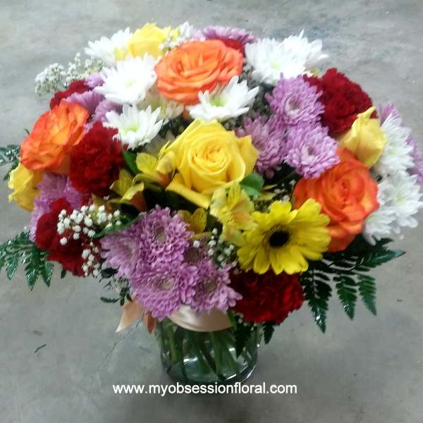 Mixed bouquet of roses, chrysanthemums, and daisies in a glass vase