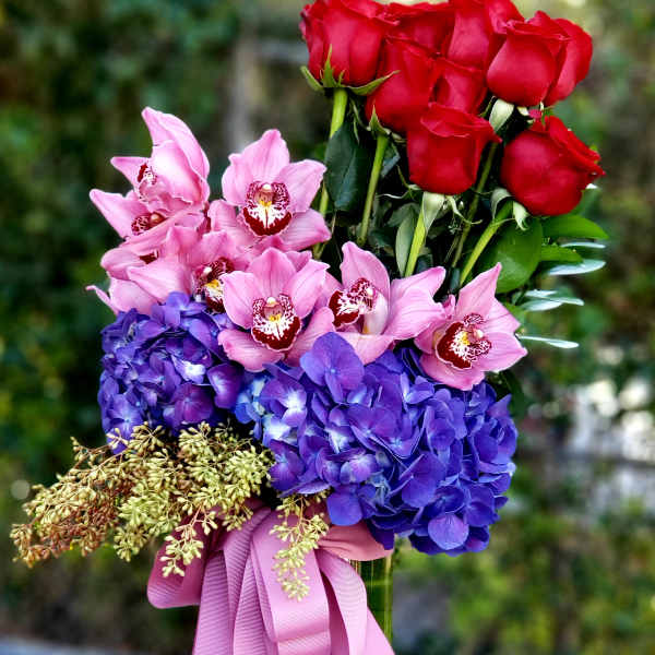 Red roses and pink orchids with purple hydrangeas in a glass vase