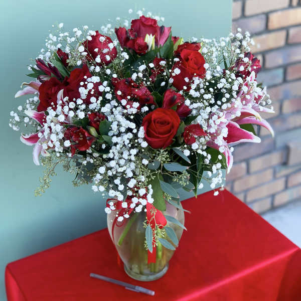 Red roses and pink lilies arranged in a glass vase with baby's breath.