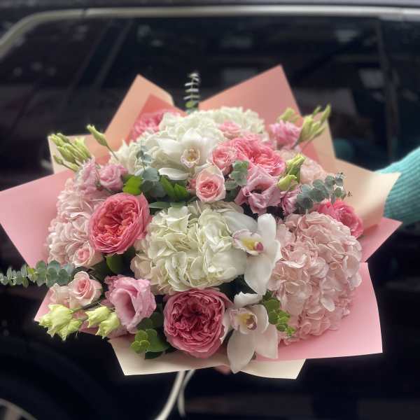 Pink and white bouquet with roses, hydrangeas, and orchids wrapped in pink paper