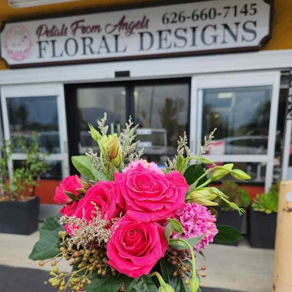 Compact arrangement of bright pink roses and mixed blooms in a small decorative vase, held outside a flower shop.