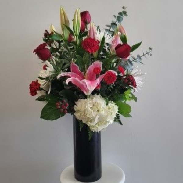 Tall bouquet of red and pink lilies, roses, and white hydrangea in a black vase