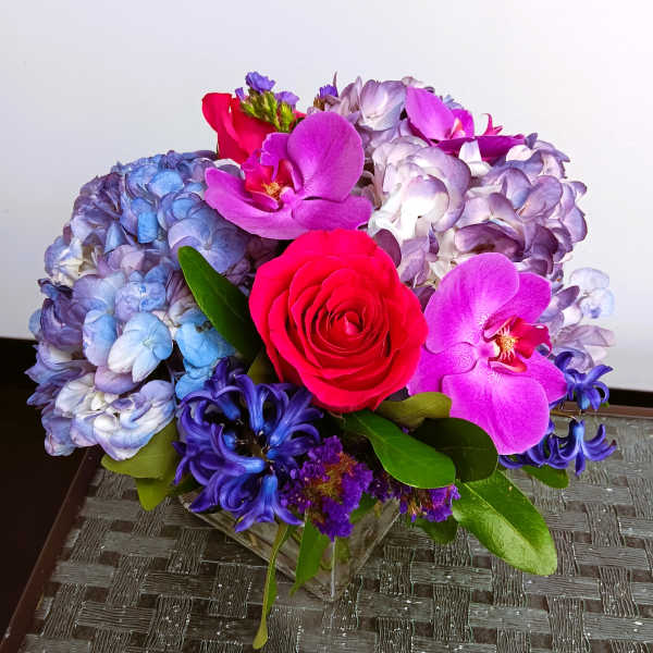 Bouquet of blue hydrangeas, pink roses, and purple orchids in a glass vase