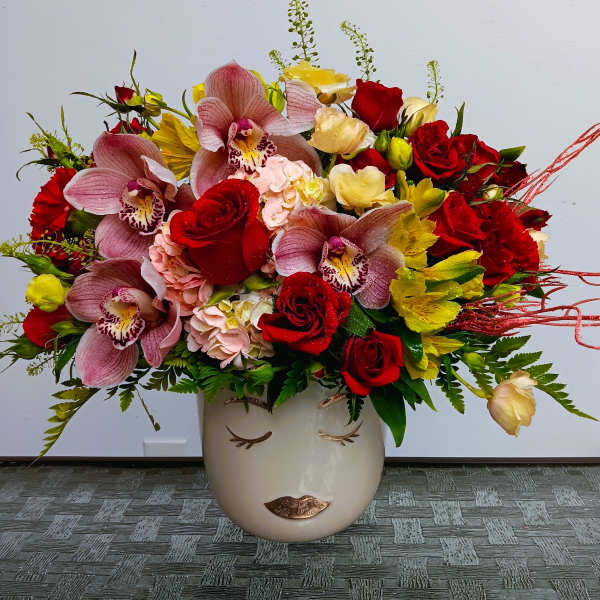 Mixed bouquet of red roses, pink orchids, and yellow flowers in a face vase
