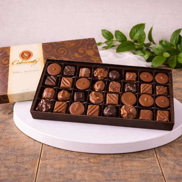 Box of assorted chocolates on a white stand with a decorative box behind it