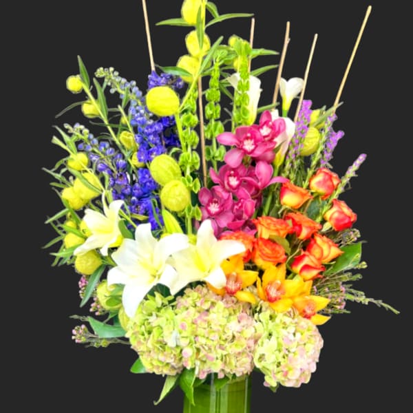 Tall mixed bouquet in a green vase with white lilies and bright orchids