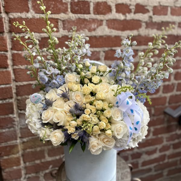Tall hatbox arrangement of ivory roses and blue flowers with baby boy ribbon accents