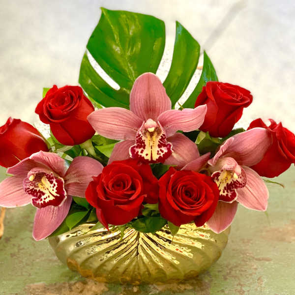 Red roses and pink orchids arranged in a gold vase