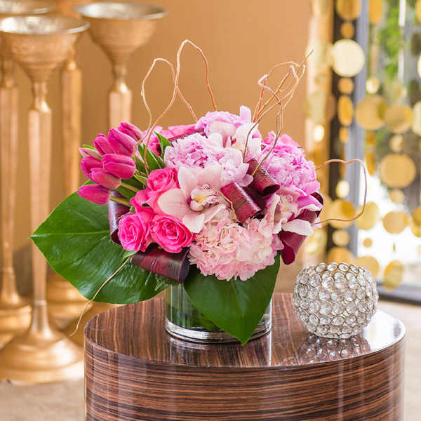 Pink floral arrangement in a clear glass vase with large green leaves
