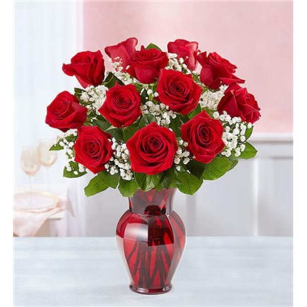 Red roses arranged in a red glass vase with white filler flowers
