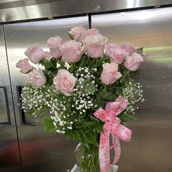 Pink roses in a glass vase with baby's breath and a pink ribbon