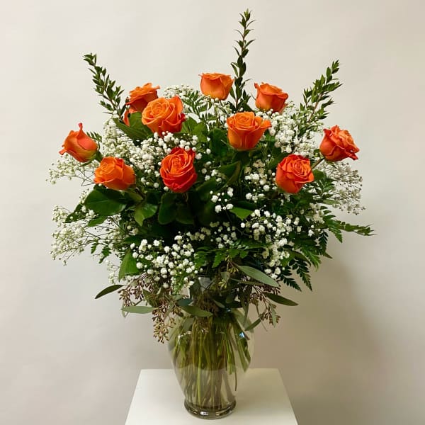 Orange roses arranged in a clear glass vase with white baby's breath