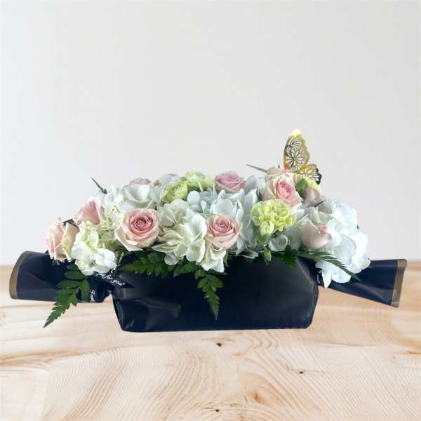 Pastel rose and hydrangea arrangement in a dark box with butterfly picks