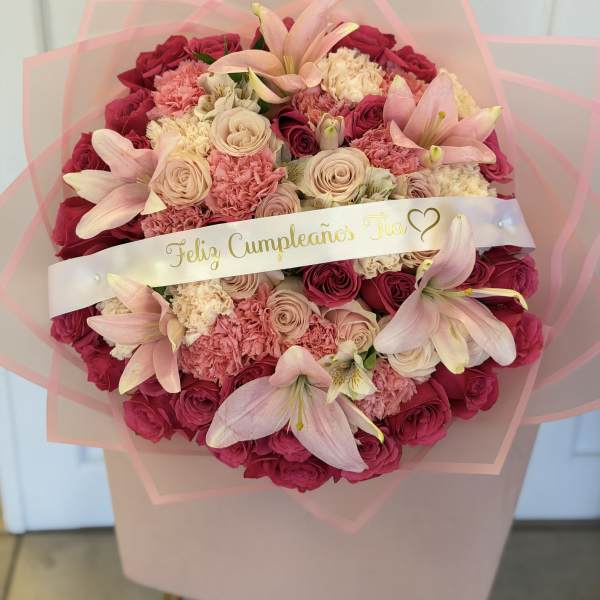 Round bouquet of pink roses, lilies, and carnations with a birthday ribbon