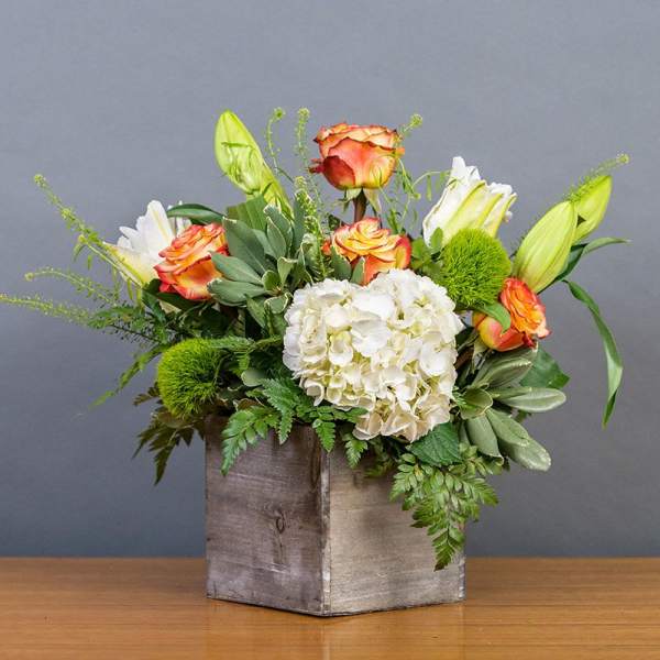 Bouquet of orange roses, white hydrangea, and lilies in a wooden box