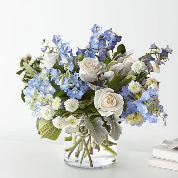 Arrangement of blue delphinium, white roses, and white mums in a clear glass vase